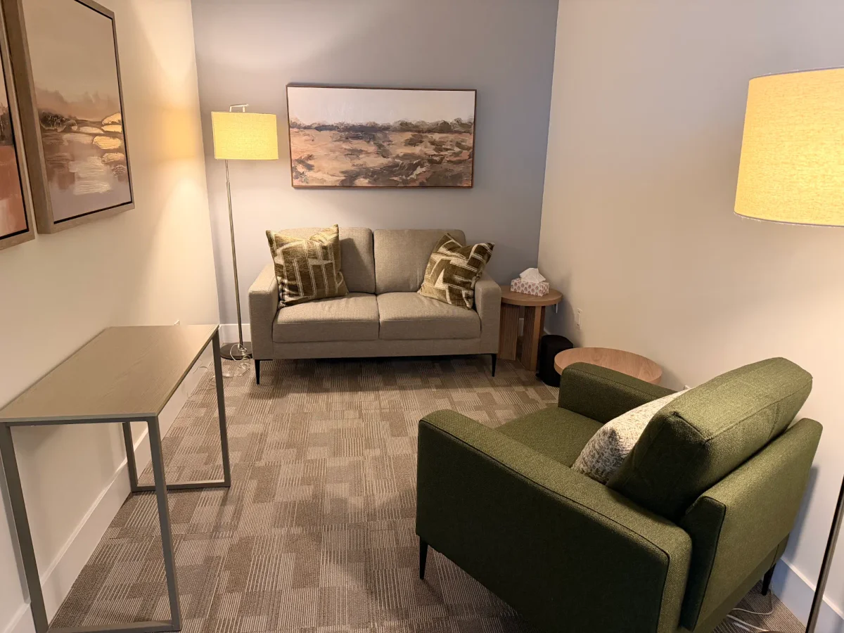 A counselling room at our Burlington office, with a loveseat, a green armchair and warm lamp light