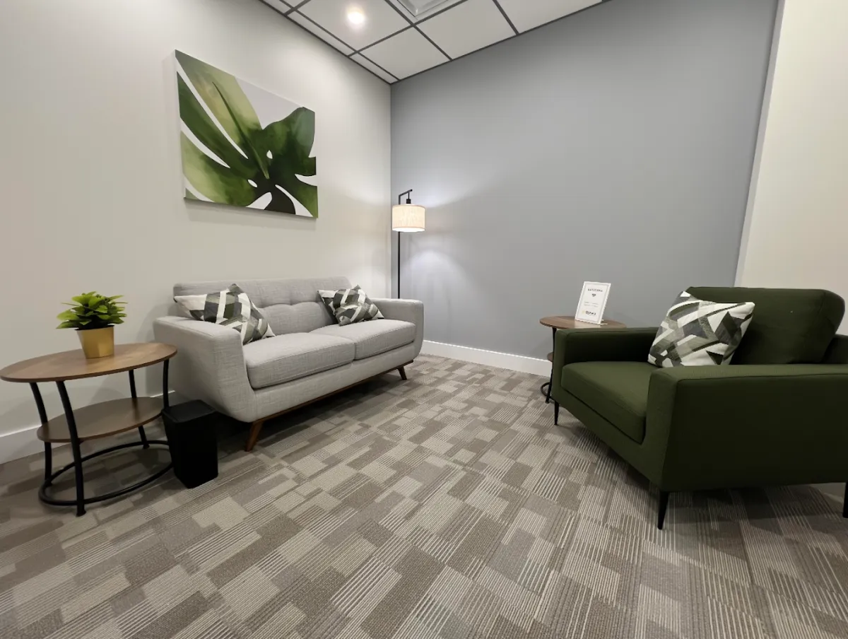 Counselling room at Graceway Wellness Burlington with a grey loveseat, green armchair, and soft lamp light